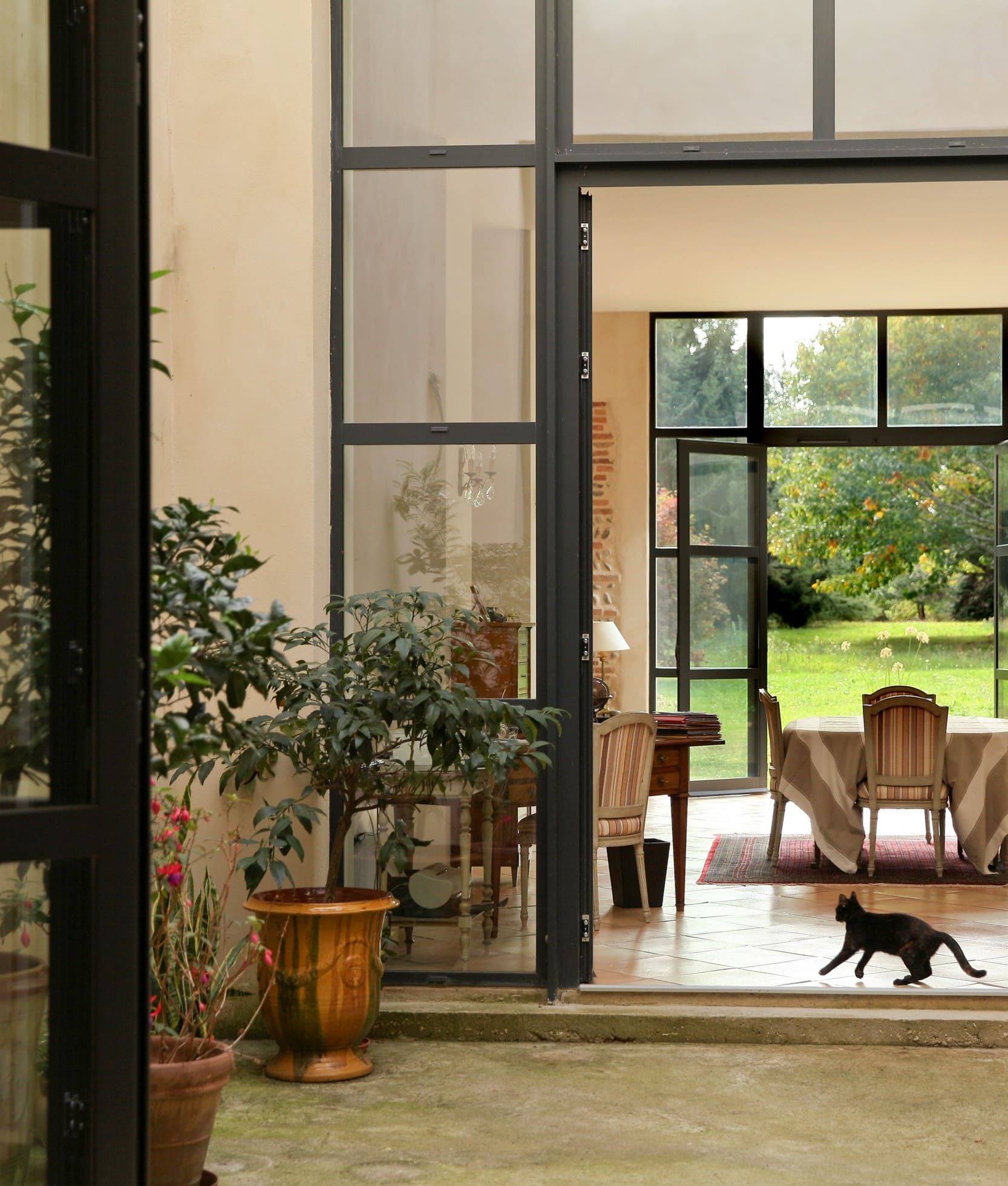 Verrière en acier ouverte sur une salle à manger et un jardin, dans une réhabilitation Bamboo Architectures