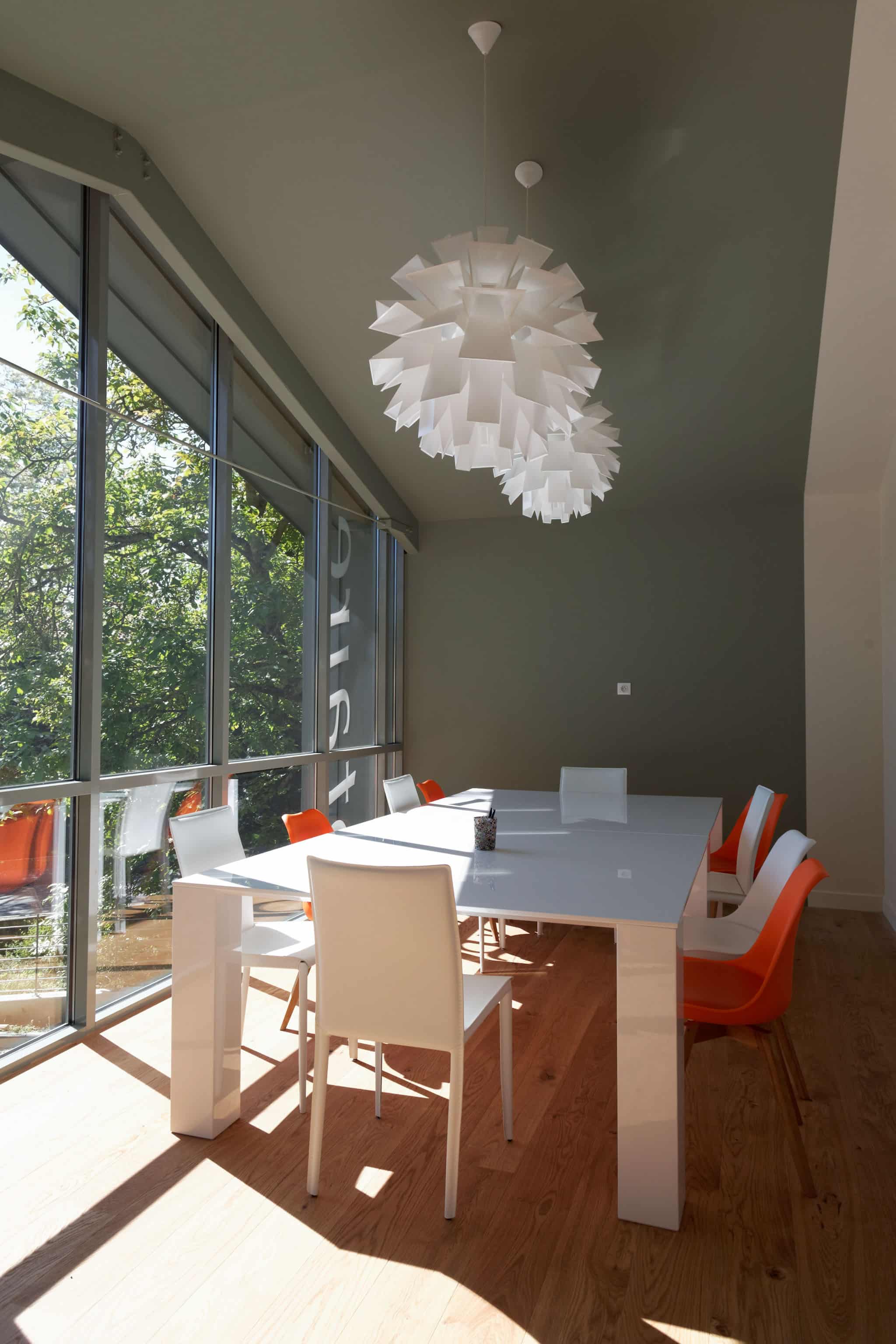 Salle à manger lumineuse aux grandes baies vitrées, mobilier blanc et touches orange