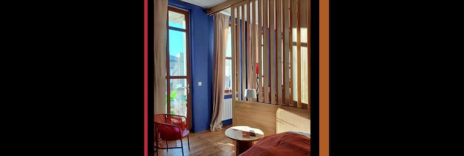 Chambre ouverte sur le balcon par une porte-fenêtre en bois, paroi ajourée en bois et mur bleu Majorelle
