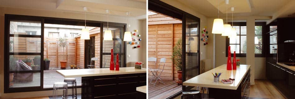 Deux vues de la pièce de vie : l'îlot blanc face aux baies coulissantes, la cuisine noire et le patio bois en enfilade