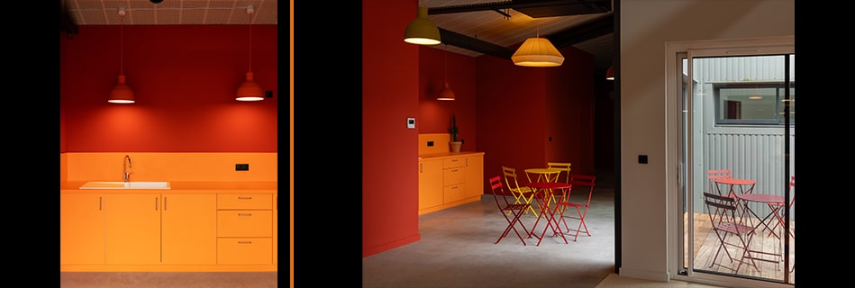 Kitchenette orange sous suspensions rouges, et salle de pause aux murs rouges ouvrant sur une terrasse par une grande baie