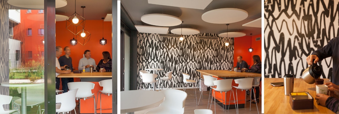 Salle de pause aux murs orange et suspensions cubiques où échange une équipe, coin repas au papier peint graphique noir et blanc sous des panneaux acoustiques ronds, et service du café