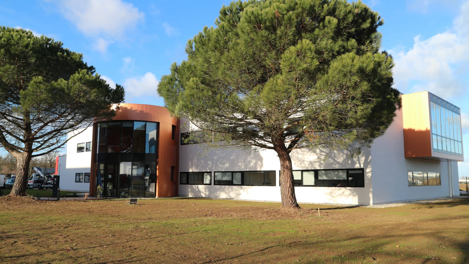 Bureaux à Plaisance : bâtiment blanc aux accents de bardage cuivré, tour d'escalier vitrée courbe et volume en surplomb, parmi les pins parasols