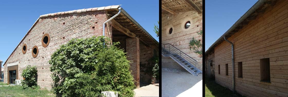 L'ancienne grange en galets et brique aux oculi ronds et sa toiture de tuiles, escalier métallique d'accès et nouvelle aile bardée de bois