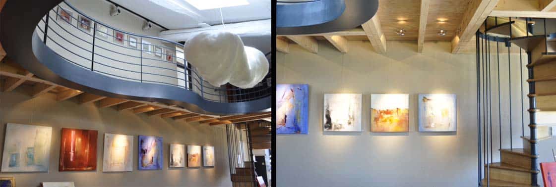 Galerie en mezzanine courbe accrochée de tableaux sous une suspension nuage, mur de peintures abstraites et escalier en colimaçon