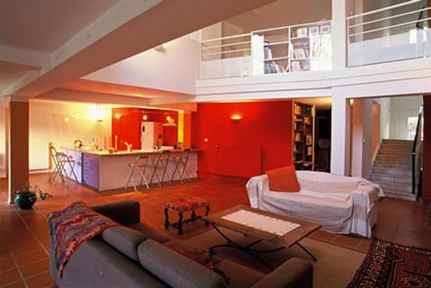 Séjour en double hauteur aux murs rouges : cuisine ouverte, mezzanine bibliothèque bordée d'un garde-corps blanc et escalier décloisonné reliant les niveaux