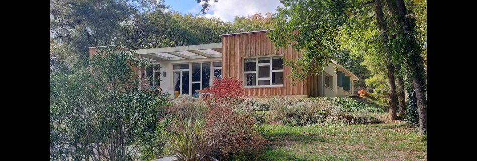 Extension contemporaine en bardage bois vertical greffée sur une maison existante, sous une pergola et de grandes baies ouvertes sur le jardin