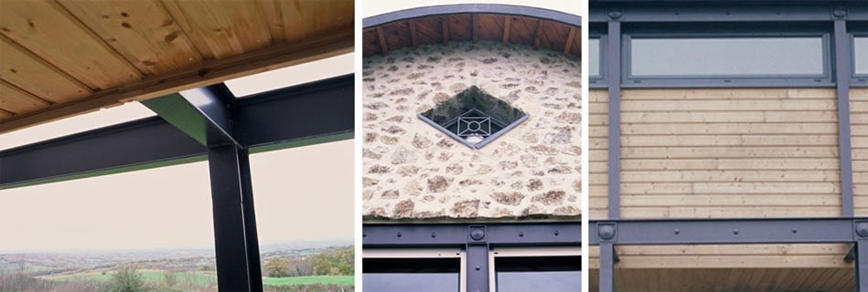 Détails d'architecture : passerelle bois et acier ouverte sur la campagne, œil-de-bœuf losangé dans le pignon en pierre, bardage bois porté par une structure acier