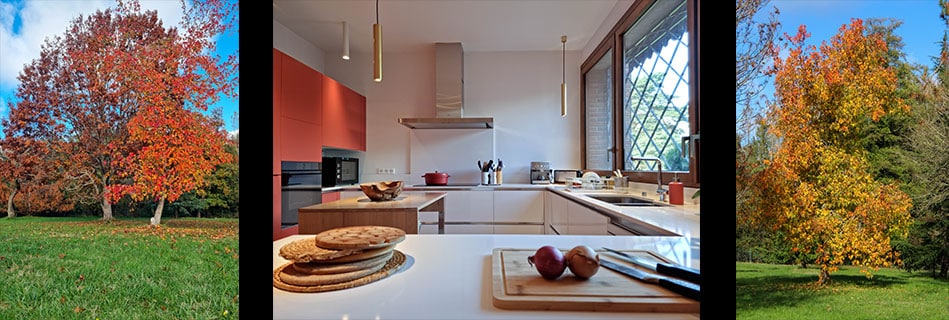 La cuisine ouverte sur le parc par la grande baie vitrée à petits carreaux, meubles terra cotta et plan de travail Silestone blanc