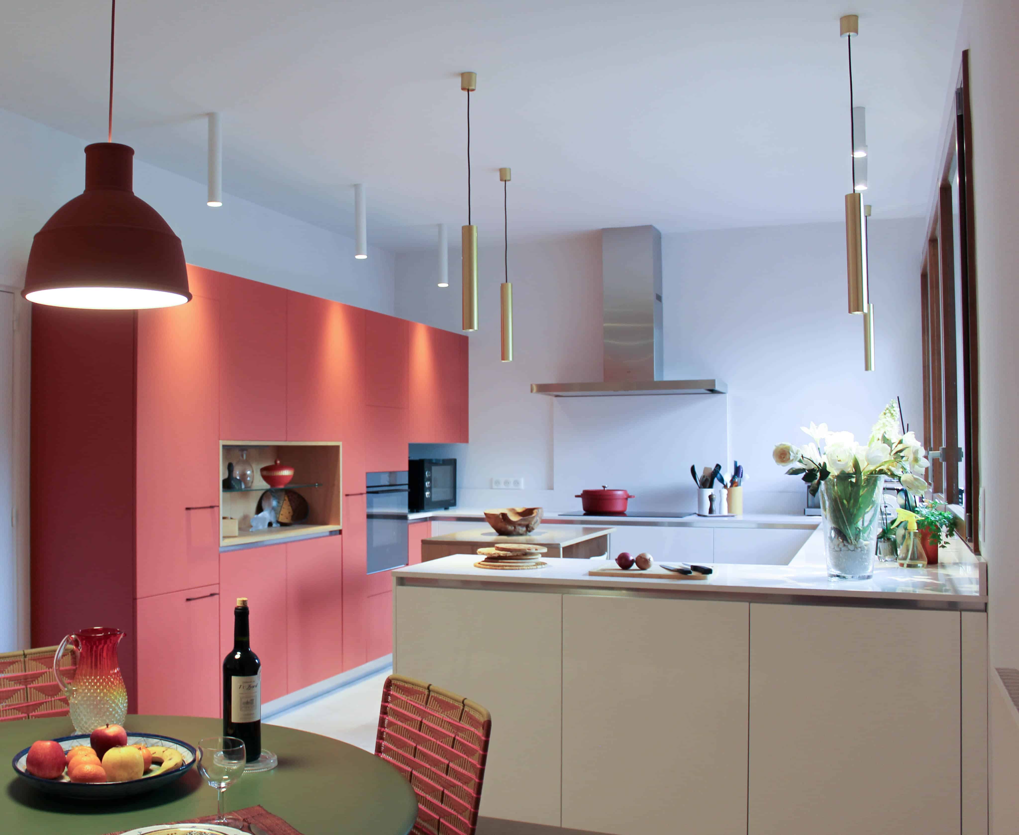 Cuisine rénovée aux meubles terra cotta et blanc cassé, îlot et coin repas rond sous des suspensions laiton et une grande lampe rouge
