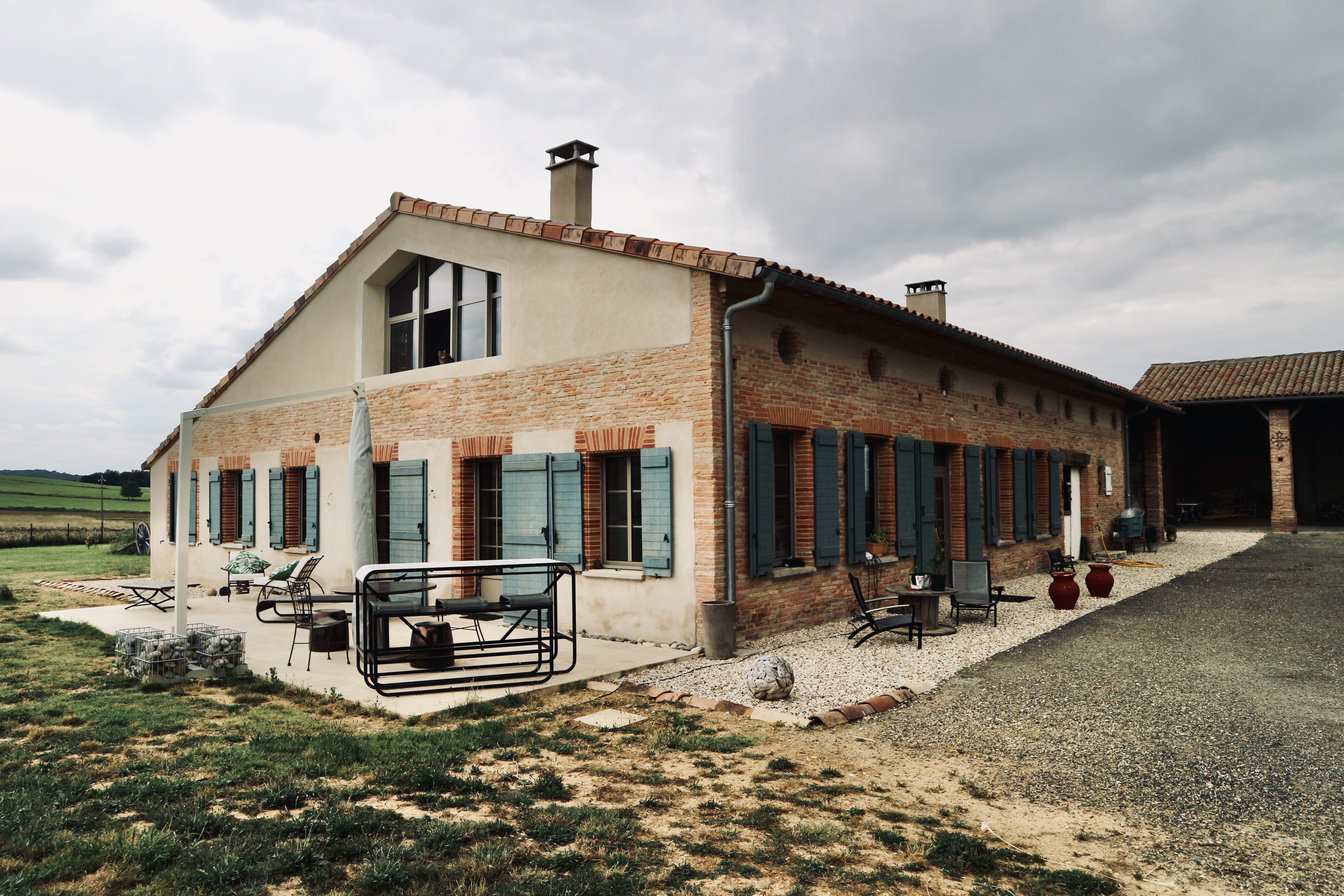Longère en briques roses de l'ancienne exploitation agricole rénovée, aux volets vert d'eau, sur une colline du nord-ouest toulousain