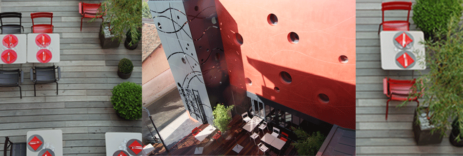 Vue plongeante sur la terrasse et ses tables, et façade de cour rouge percée d'oculi et de panneaux découpés