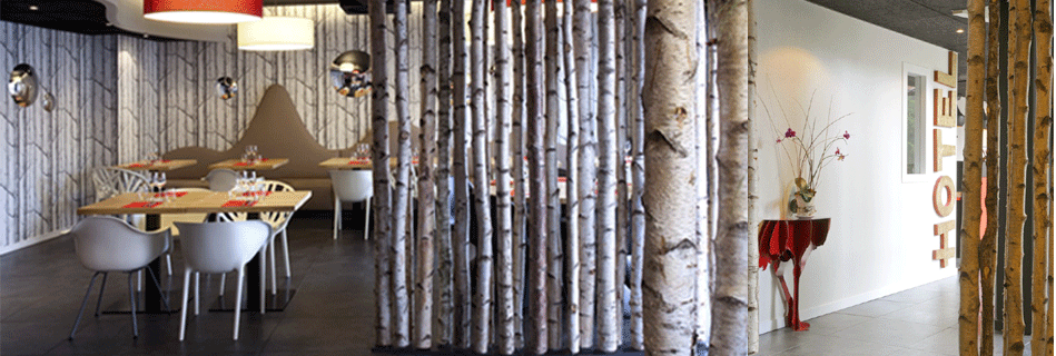 Salle de restaurant à cloison de rondins de bouleau, papier peint forêt et banquettes en silhouette de montagne sous des suspensions rouges