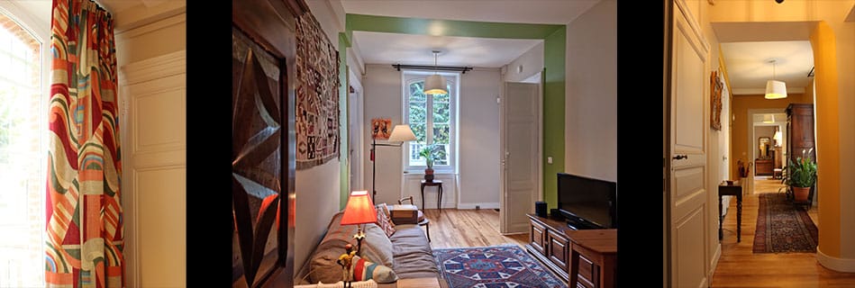Salon de l'appartement rénové : rideaux à motifs colorés, canapé et tapis ancien devant une fenêtre sur les arbres, enfilade vers un couloir chaleureux