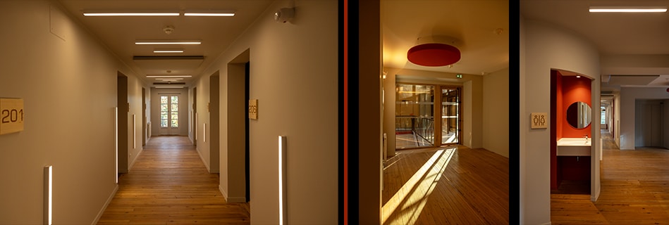Couloir d'hébergement aux portes de chambres numérotées et parquet, plafonnier rouge près de l'accès vitré et niche lavabo rouge