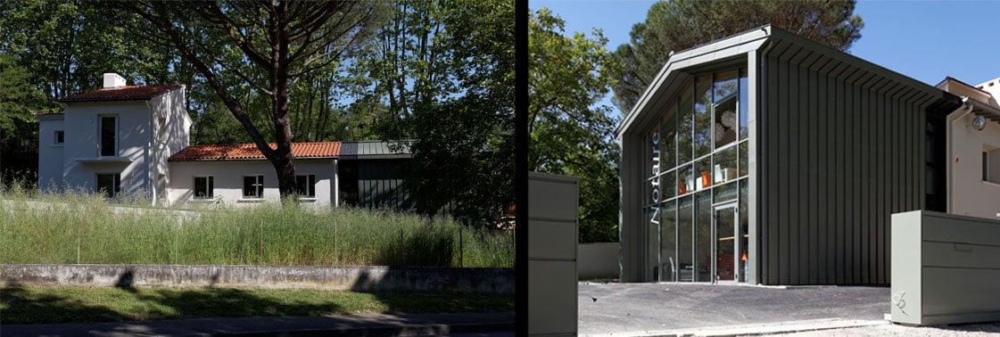 La maison blanche existante et son extension le long de la route bordée de roseaux, et le nouveau volume anguleux à bardage métallique portant l'inscription Notaire sur sa façade vitrée