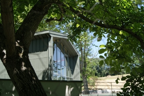 Office notarial de Ramonville : volume contemporain à bardage métallique gris-vert et grand pignon vitré, aperçu à travers les arbres