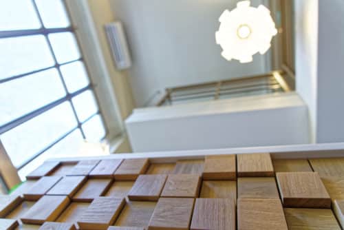 Détail d'un mur en tasseaux de bois en relief près d'un escalier de l'office notarial, sous une suspension design et une fenêtre à croisillons