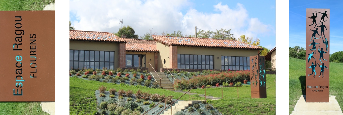 Signalétique en acier corten « Espace Ragou » aux silhouettes de jeunes découpées, et façade du pôle jeunesse à toiture de tuiles et larges baies sur le jardin fleuri