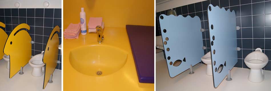 Sanitaires des enfants : cabinets séparés par des cloisons ludiques jaunes et bleues, vasque jaune à hauteur d'enfant sur carrelage bleu nuit