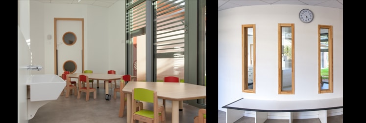 Salle d'activités aux tables et chaises à hauteur d'enfant, porte à hublots ronds et cloison vitrée, et pièce courbe éclairée par trois fenêtres verticales encadrées de bois
