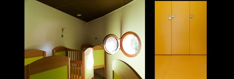 Dortoir aux petits lits en bois sous un plafond sombre, éclairé par deux hublots ronds, et rangements jaunes toute hauteur