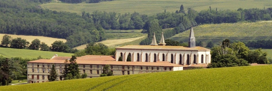 Le monastère et son église dans la campagne vallonnée, longue façade et clocher au milieu des champs