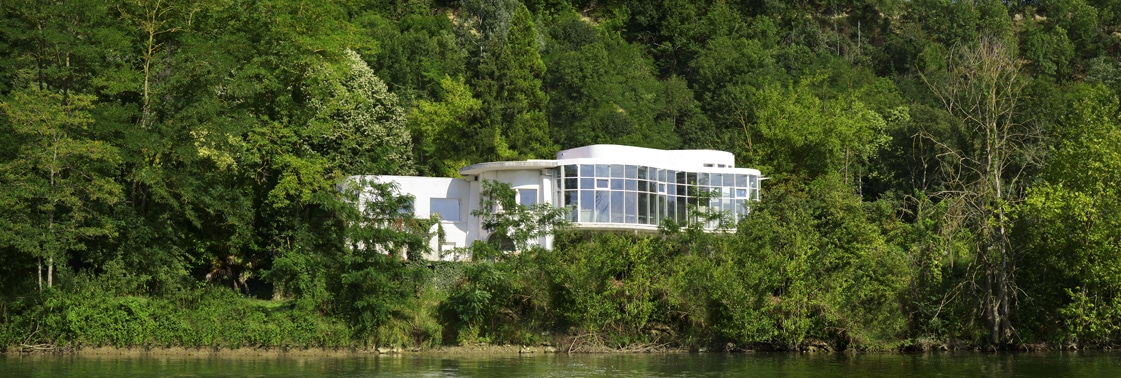 Le restaurant tout blanc niché dans la verdure au bord de la rivière, vu depuis l'autre rive