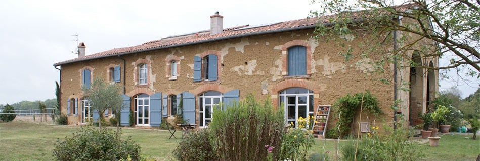 Façade extérieure de la ferme en pierre et brique aux volets bleus, longue bâtisse agricole restaurée dans le domaine