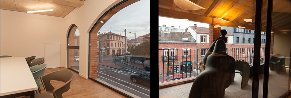 Salle de réunion de l'étage à plafond bois et grande baie cintrée sur la rue, et terrasse ouverte sur les toits toulousains
