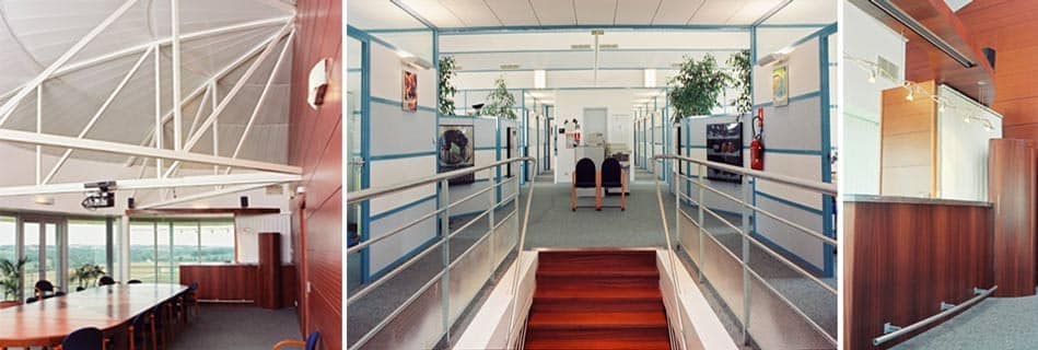 Salle de réunion sous la charpente rayonnante, bureaux en mezzanine aux garde-corps d'acier bleu et cloisons vitrées, et banque d'accueil en bois
